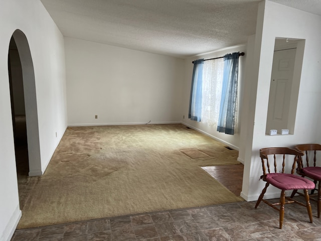 carpeted spare room with baseboards, arched walkways, and a textured ceiling