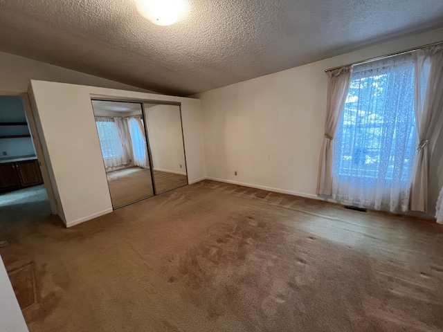 unfurnished bedroom with visible vents, lofted ceiling, carpet, a textured ceiling, and a closet