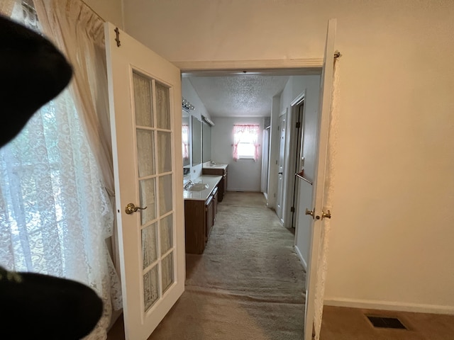 hall featuring visible vents, carpet flooring, a sink, a textured ceiling, and baseboards