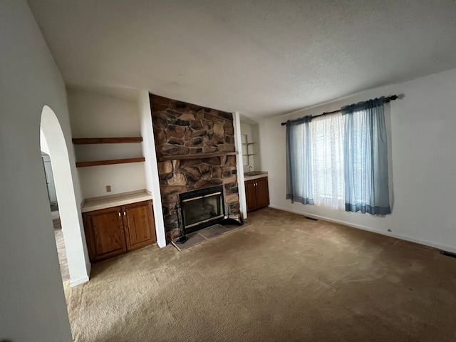 unfurnished living room featuring carpet, arched walkways, a textured ceiling, and a stone fireplace