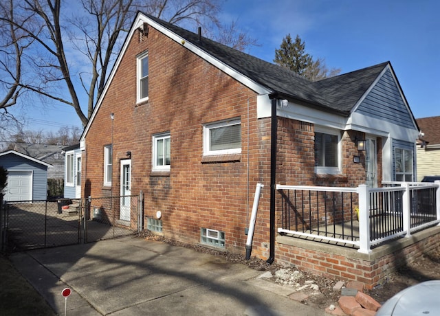 view of side of property with brick siding, an outdoor structure, driveway, roof with shingles, and a gate