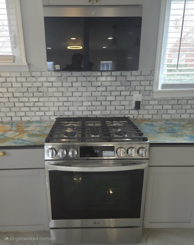 kitchen featuring tasteful backsplash, stainless steel range with gas stovetop, plenty of natural light, and exhaust hood