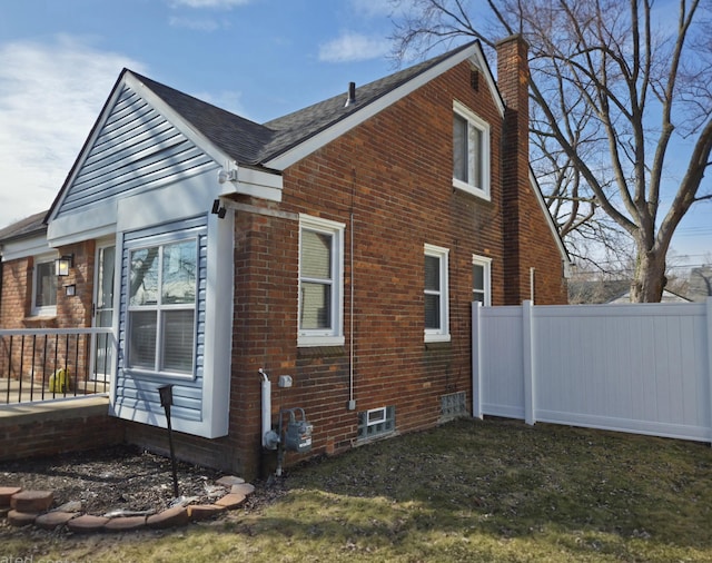 view of side of home featuring roof with shingles, brick siding, a chimney, and fence