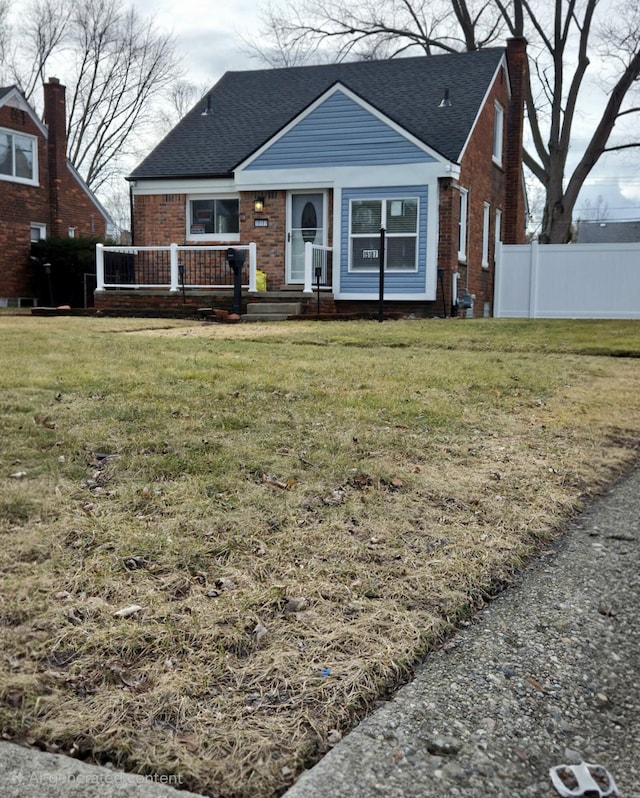 view of front of house with brick siding, roof with shingles, a chimney, a front yard, and fence