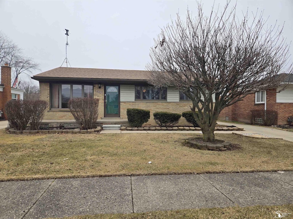 ranch-style home with brick siding, a front lawn, and roof with shingles