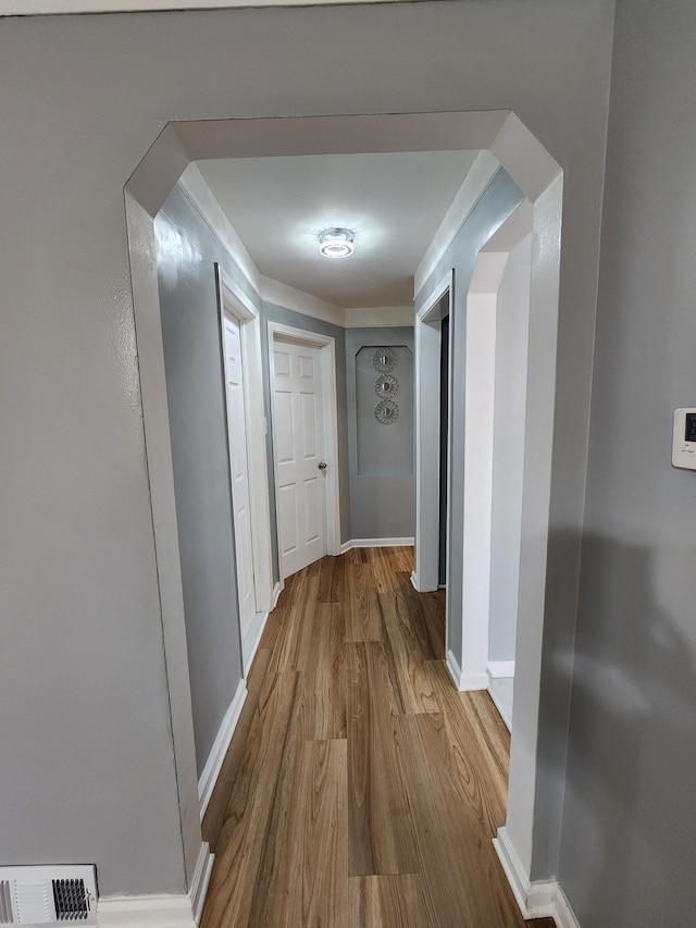 hallway featuring visible vents, arched walkways, baseboards, and wood finished floors