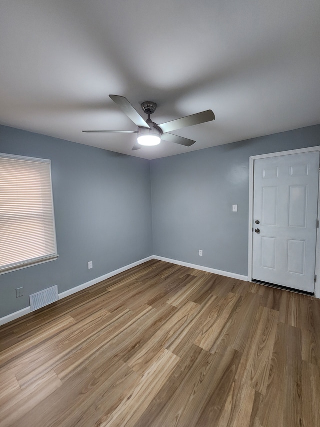 empty room featuring a ceiling fan, wood finished floors, visible vents, and baseboards