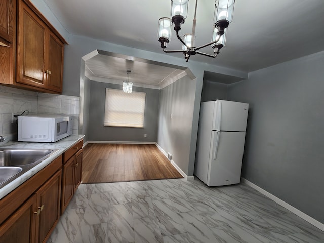 kitchen featuring arched walkways, a notable chandelier, brown cabinets, and white appliances