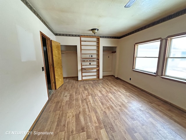 unfurnished bedroom with wood finished floors, baseboards, and two closets