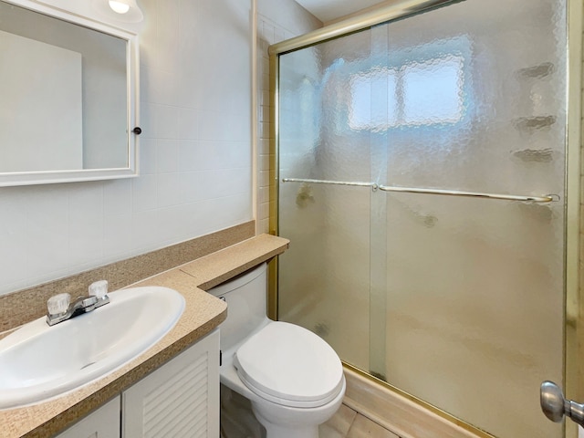 bathroom with toilet, vanity, a shower stall, and tile walls