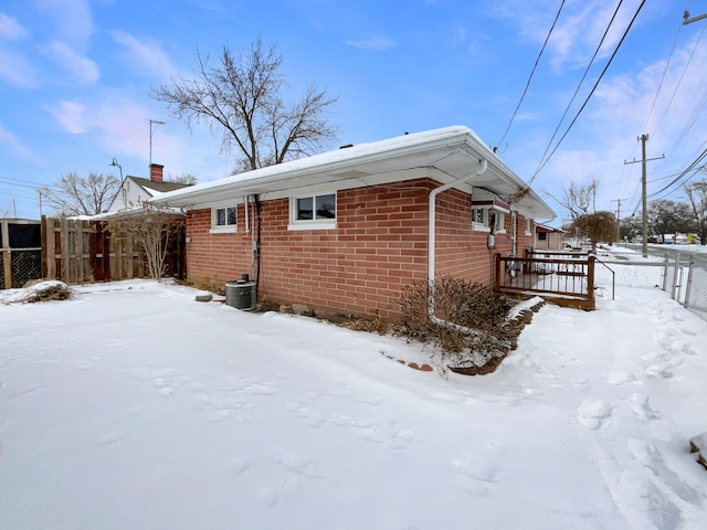 view of snow covered exterior featuring brick siding and fence