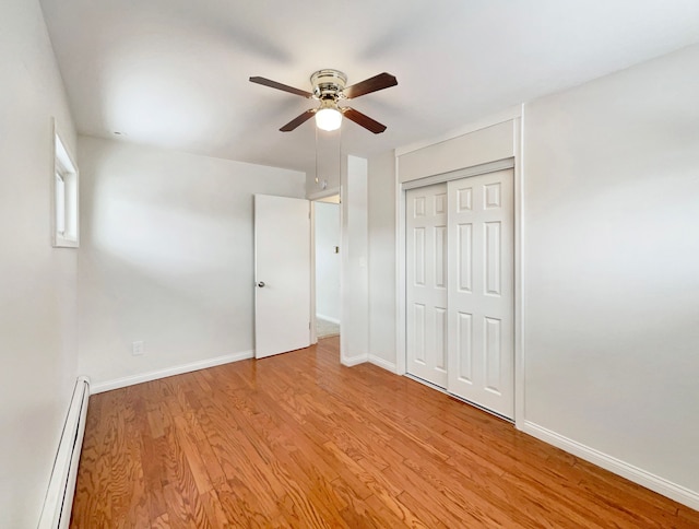 unfurnished bedroom with a closet, baseboard heating, ceiling fan, wood finished floors, and baseboards