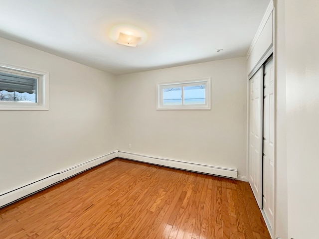 unfurnished bedroom featuring light wood finished floors, a baseboard heating unit, and a closet