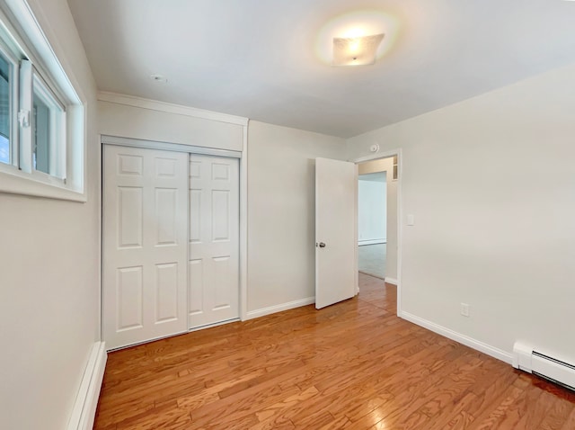 unfurnished bedroom featuring a baseboard heating unit, baseboards, baseboard heating, light wood-type flooring, and a closet