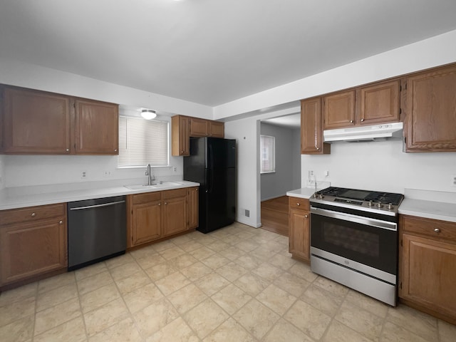 kitchen with brown cabinetry, stainless steel appliances, light countertops, under cabinet range hood, and a sink