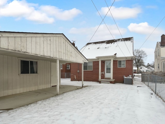 snow covered back of property with entry steps, brick siding, central AC unit, and fence