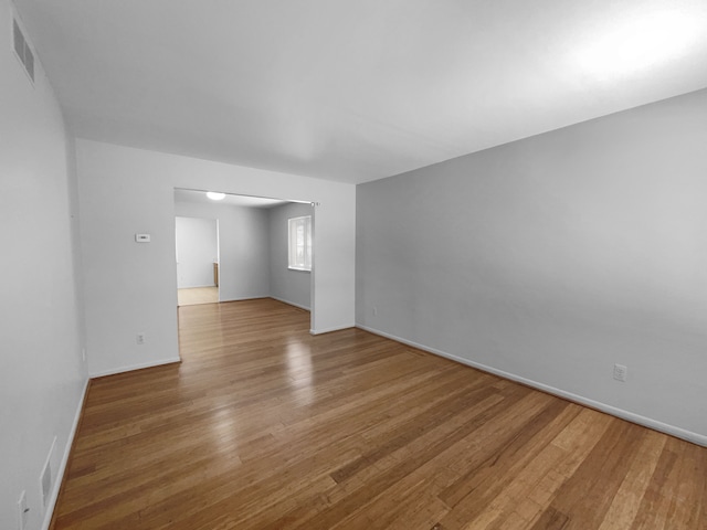 spare room with wood finished floors, visible vents, and baseboards