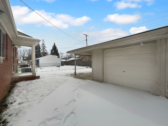 snow covered garage featuring a garage and fence