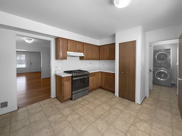 kitchen featuring stacked washer and clothes dryer, light countertops, stainless steel gas stove, under cabinet range hood, and baseboards