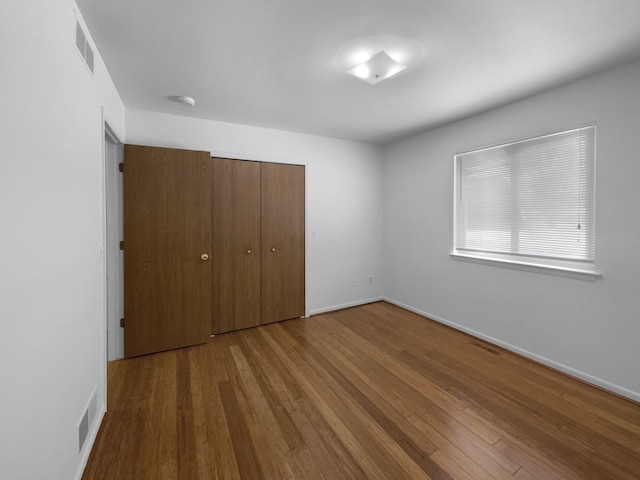 unfurnished bedroom with a closet, wood finished floors, and visible vents