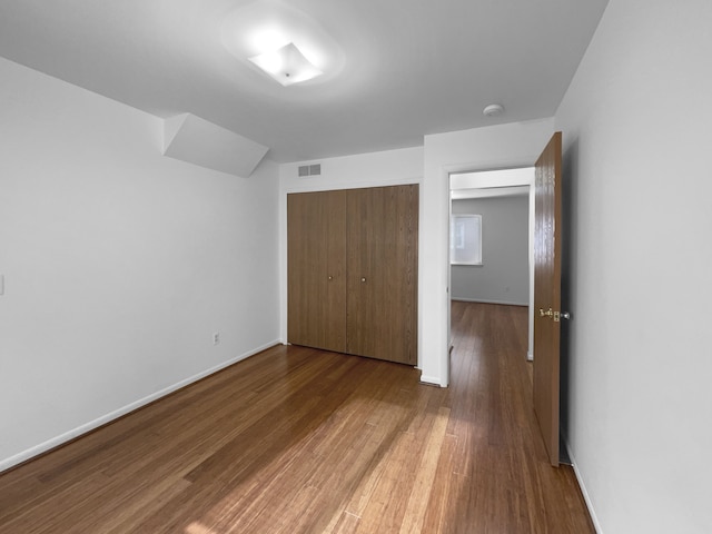 unfurnished bedroom featuring baseboards, visible vents, a closet, and wood finished floors