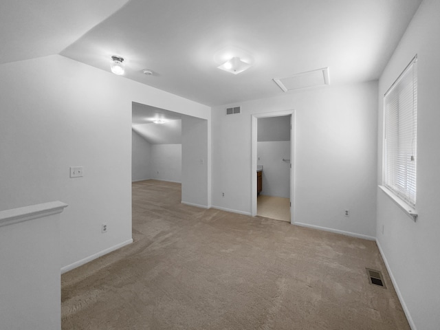 carpeted empty room featuring attic access, lofted ceiling, visible vents, and baseboards