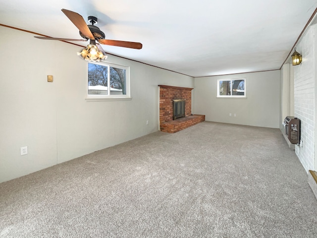 unfurnished living room with a ceiling fan, a brick fireplace, carpet flooring, and heating unit