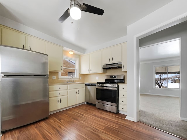 kitchen with dark wood-style floors, appliances with stainless steel finishes, cream cabinets, under cabinet range hood, and a sink