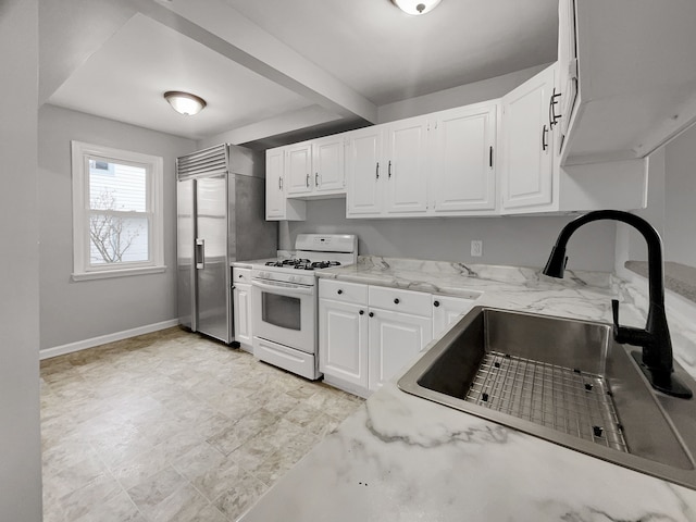 kitchen with white gas range oven, baseboards, white cabinets, light stone countertops, and a sink