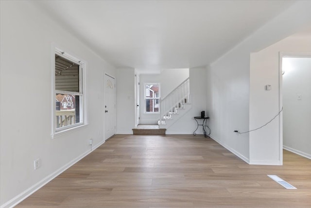 entryway featuring baseboards, light wood finished floors, and stairs