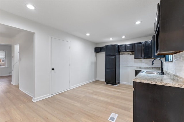 kitchen with light wood-style floors, tasteful backsplash, visible vents, and a sink