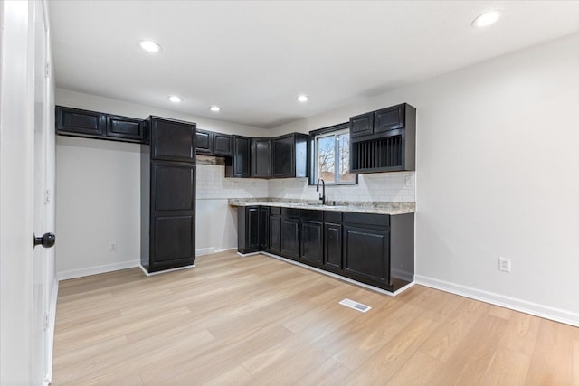 kitchen featuring tasteful backsplash, light wood-type flooring, dark cabinetry, and baseboards