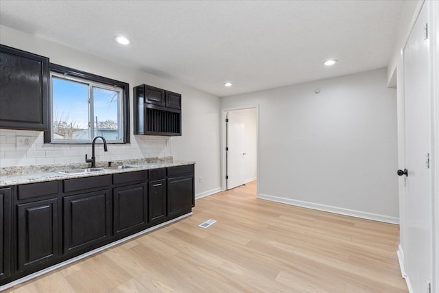 kitchen with light wood-style floors, dark cabinetry, backsplash, and a sink