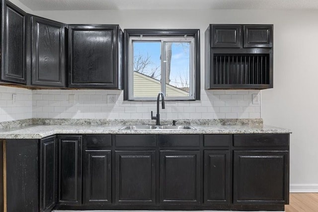 kitchen featuring light wood finished floors, decorative backsplash, a sink, dark cabinets, and baseboards