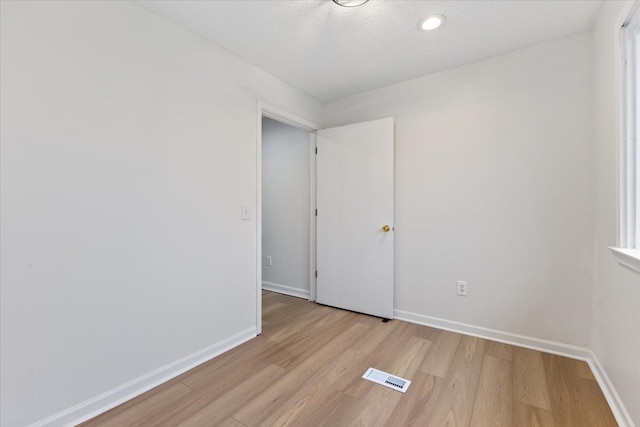 spare room featuring light wood-type flooring, visible vents, a textured ceiling, and baseboards