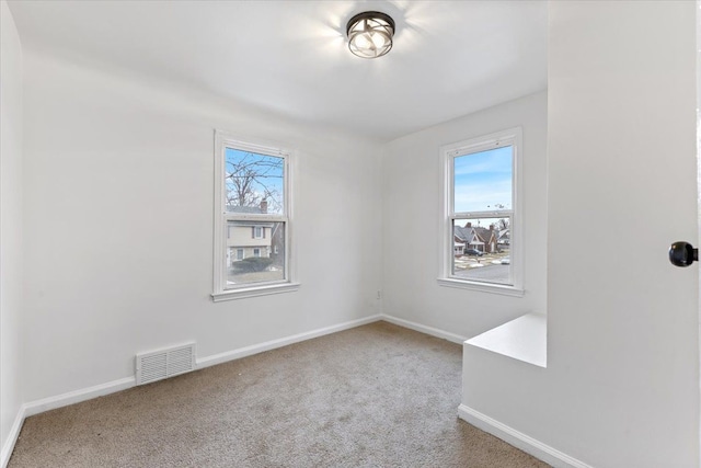 spare room featuring carpet floors, a wealth of natural light, visible vents, and baseboards