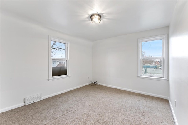 spare room featuring carpet floors, visible vents, plenty of natural light, and baseboards