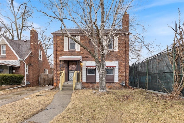 view of front of home with brick siding, a chimney, a front yard, and fence