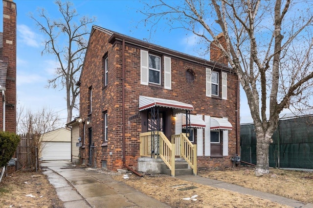 view of front of property with brick siding, a detached garage, a chimney, and an outbuilding