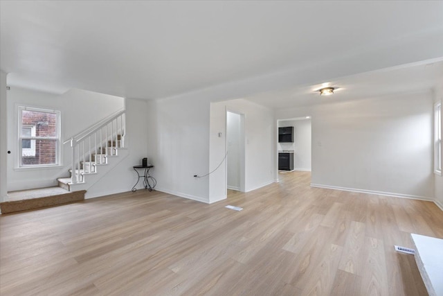 unfurnished living room with stairs, baseboards, and light wood-style floors