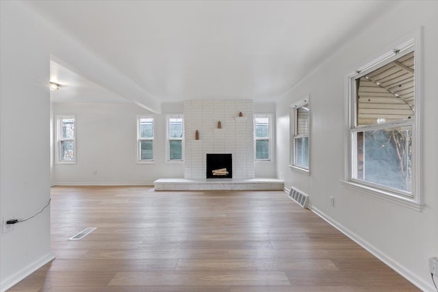 unfurnished living room featuring baseboards, a brick fireplace, visible vents, and light wood-style floors