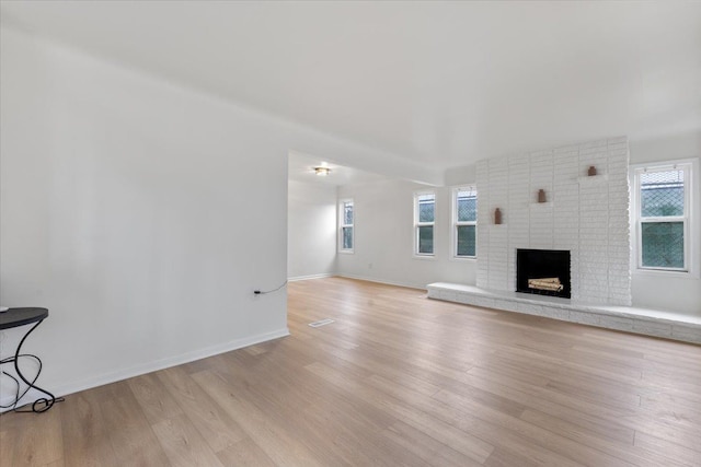 unfurnished living room with light wood-type flooring, a brick fireplace, and baseboards