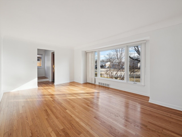 spare room with light wood-type flooring, visible vents, and baseboards