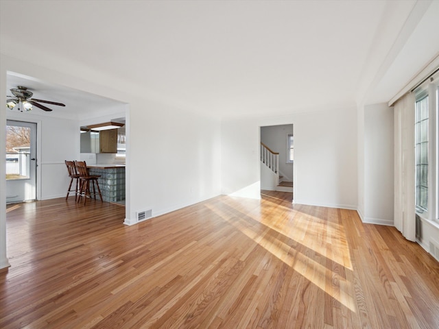 unfurnished living room with ceiling fan, stairs, visible vents, and wood finished floors