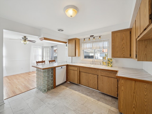 kitchen with tile countertops, a peninsula, a sink, brown cabinets, and dishwasher