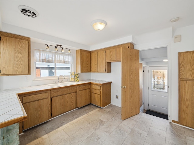 kitchen with brown cabinets, visible vents, a sink, and tile countertops