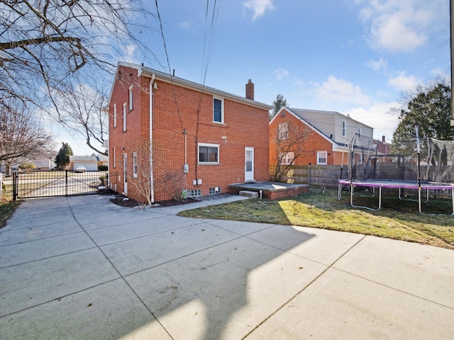 rear view of property featuring a trampoline, brick siding, a yard, a chimney, and fence