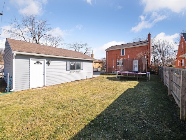 rear view of property featuring a trampoline, fence, and a lawn