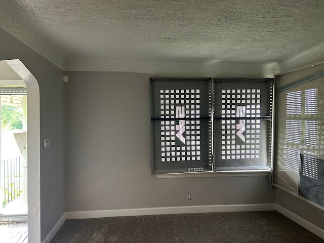 carpeted spare room featuring baseboards, arched walkways, and a textured ceiling