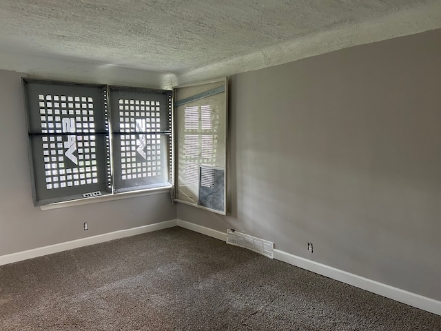 spare room featuring dark colored carpet, visible vents, a textured ceiling, and baseboards